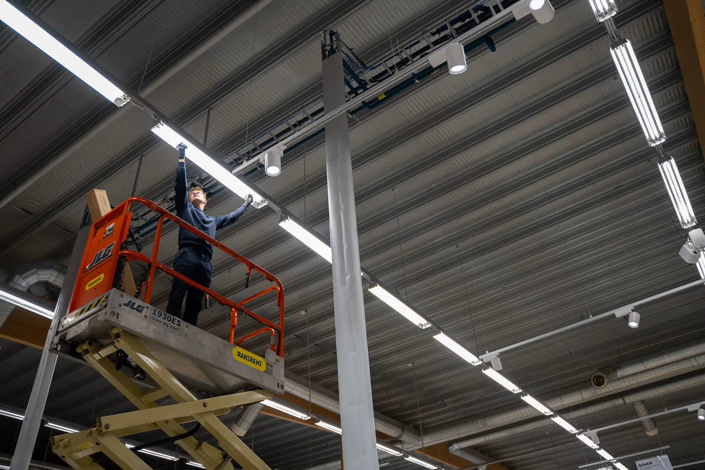 Greenmorals installatörer byter belysning i lagerhall från saxlift